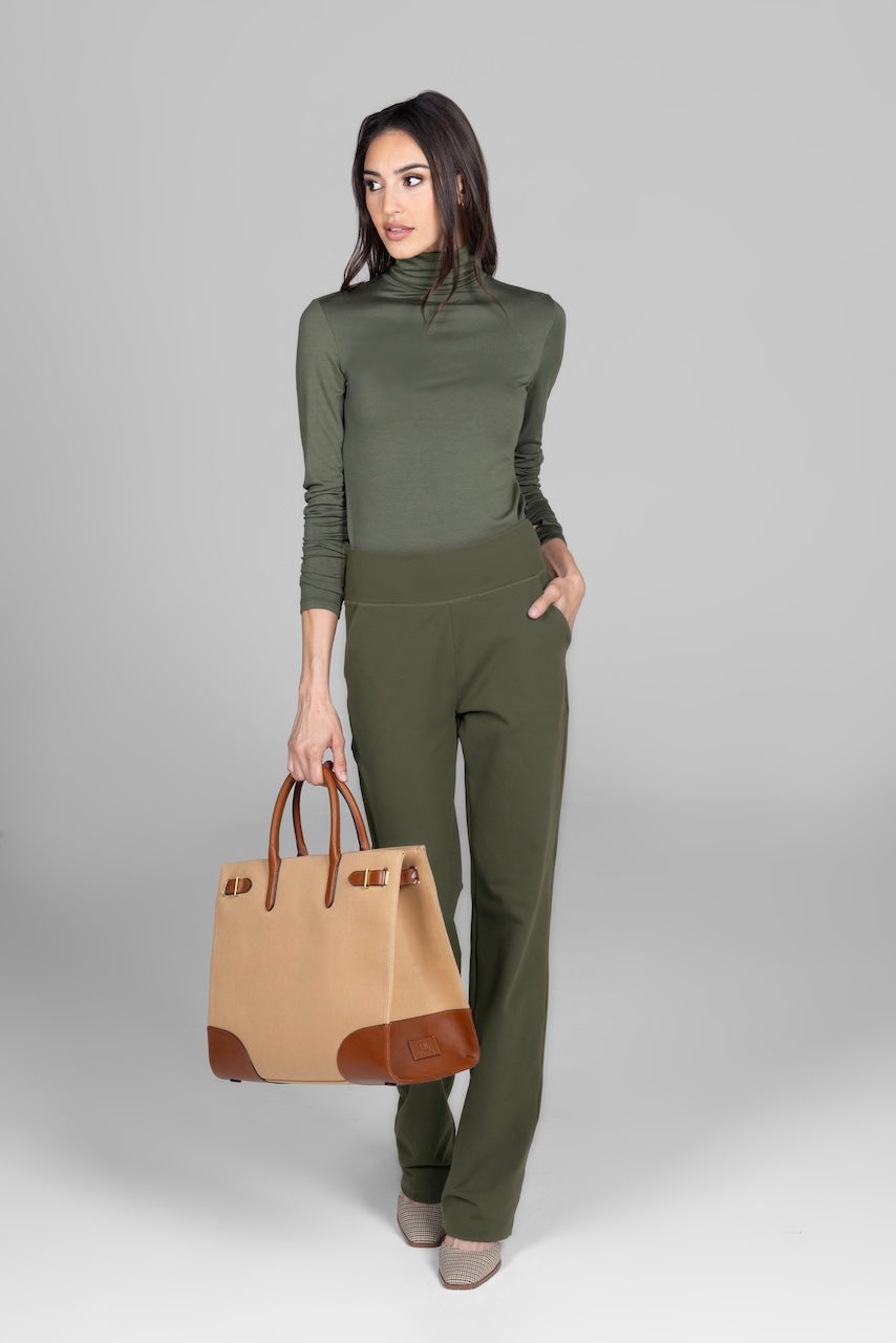 Woman in olive turtleneck and pants holding a tan handbag.