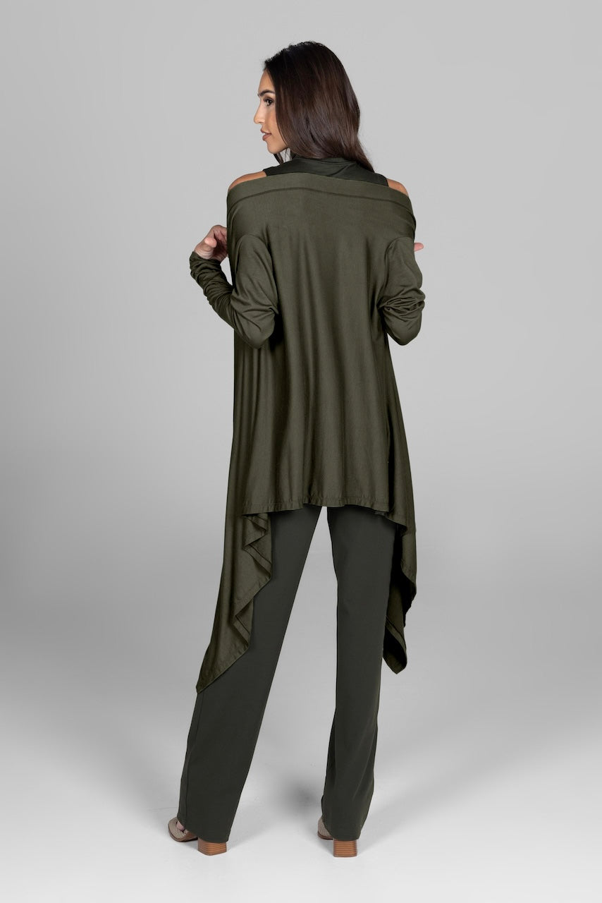 Back view of a woman wearing a dark green infinity wrap over matching pants and a sleeveless turtleneck, showing the flowing design of the wrap.